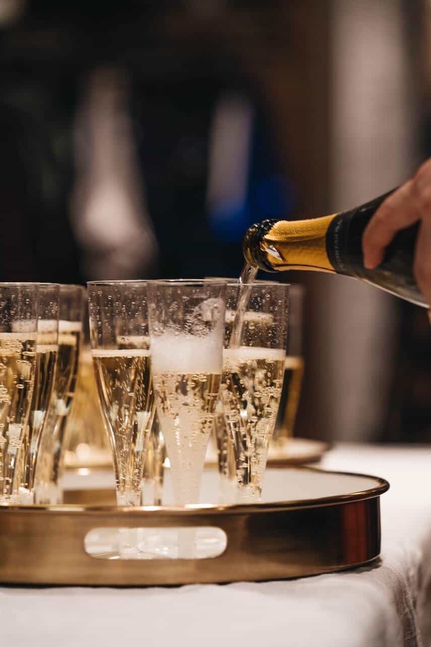 Champagne Trivia Questions and Answers image of champagne flutes on a round serving platter, being filled by a bottle