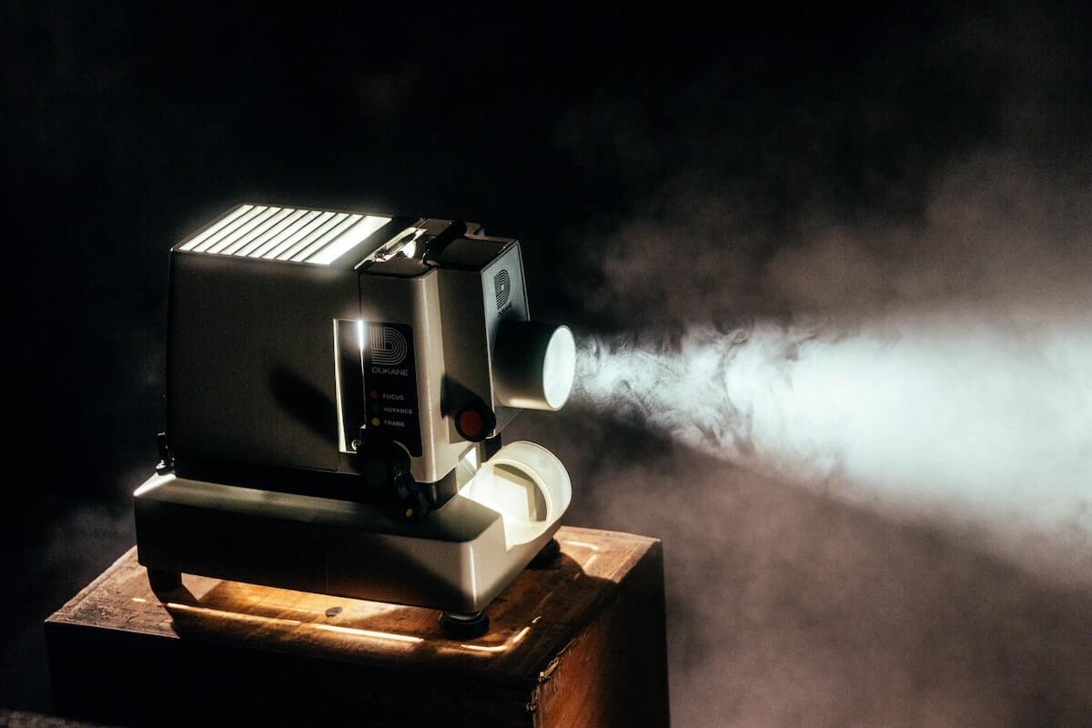 80s Movie Trivia Questions and Answers cover photo of a large black projector on a wooden table, light coming from the lens
