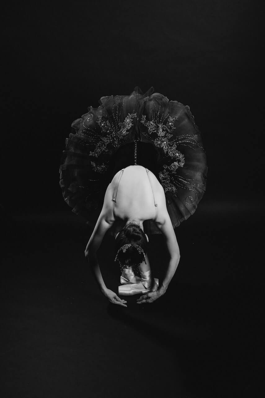 Ballerina in a black tutu bent in half taking a bow