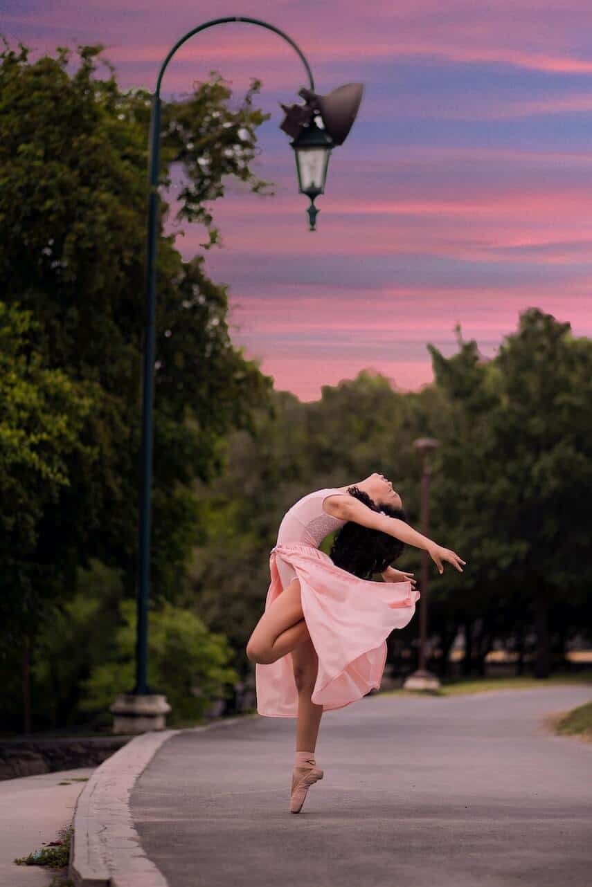 Ballerina in a pink leotard with pink chiffon skirt dancing in a park