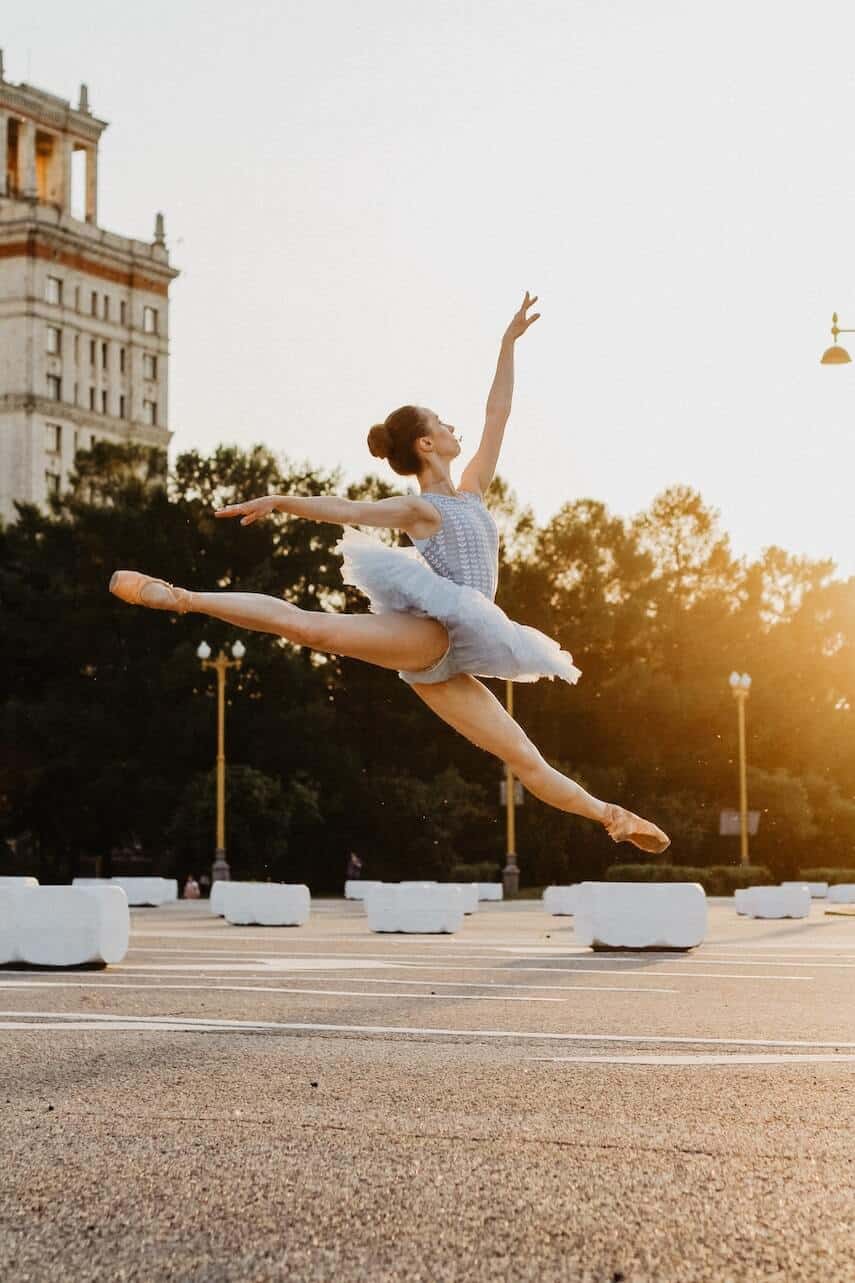 Ballerina leaping in the air in split in an empty car park in front of a multi storey building