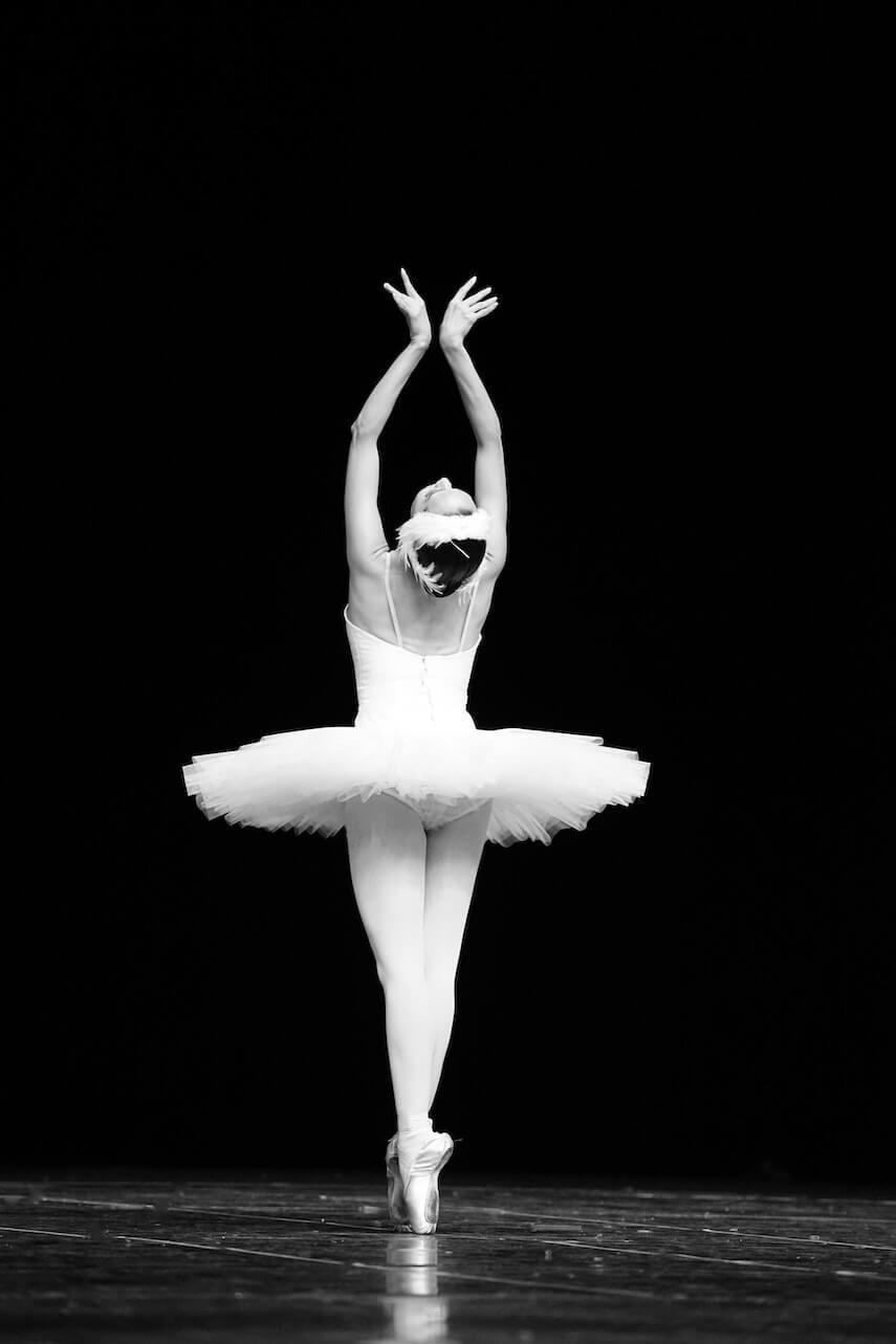 Ballerina on stage in white tutu, on pojnte, her arms above her head