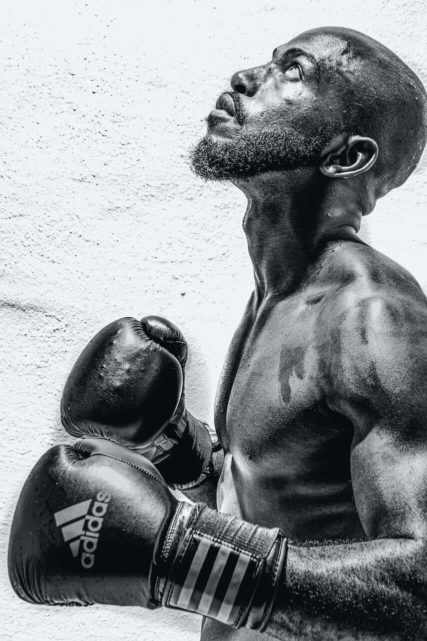 Black and White photo of a shirtless muscly black man wearing black adidas boxing gloves