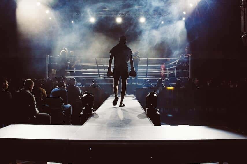 Boxer walking down a raised platform towards the boxing ring lit up by spotlights