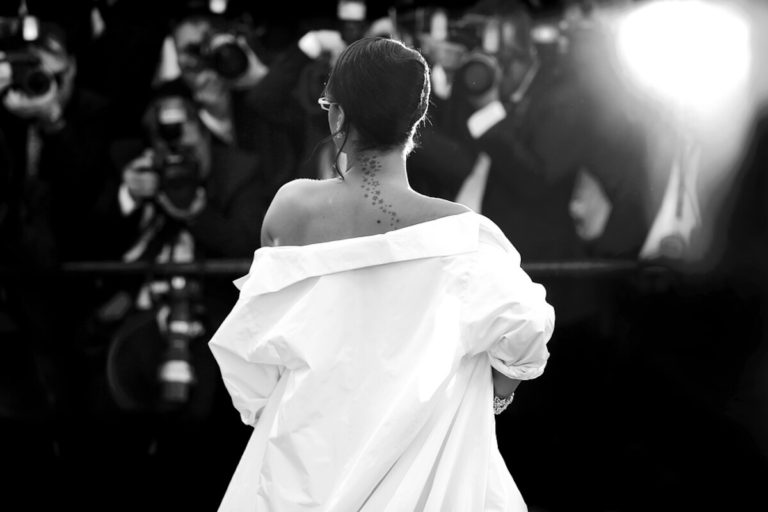 Famous people anagrams with answers cover photo og a woman wearing a white open shirt with her back to the camera facing a line of paparazzi cameras on the red carpet