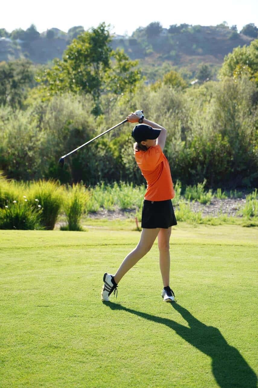 Female golfer wearing an orange shirt and black skirt, at the end of her swing