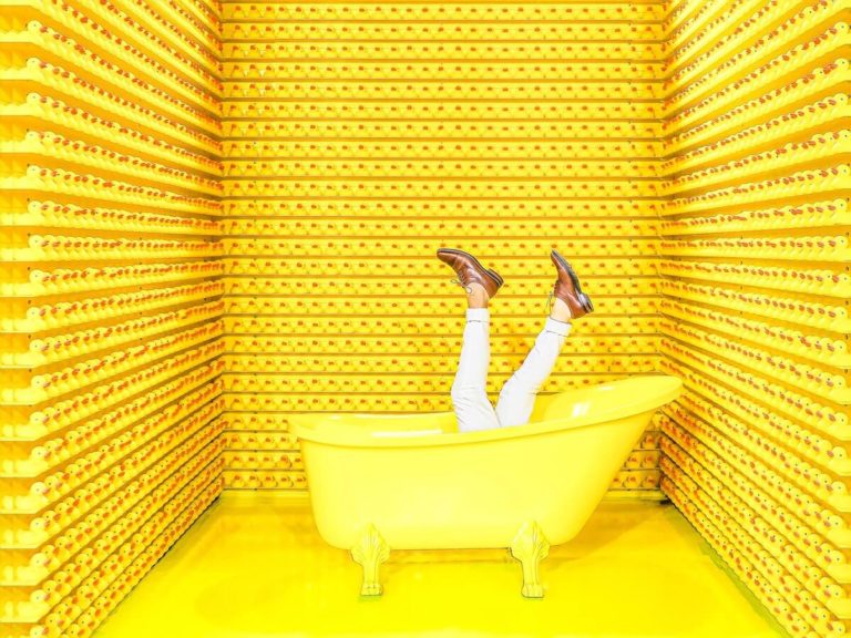 Funny Anagrams with Answers cover photo of a mans legs in white jeans sticking out of a yellow bathtub in a room whose walls are lined with yellow rubber ducks