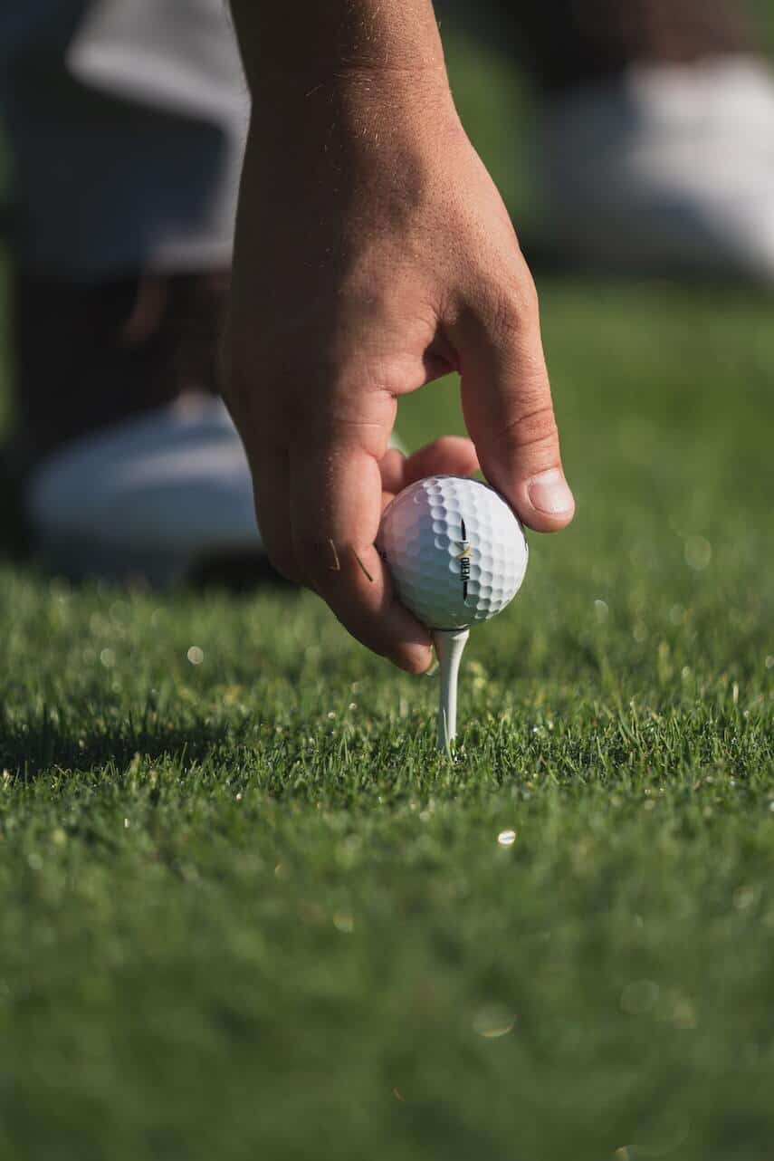 Hand placing a golf ball onto a white tee raised above the ground