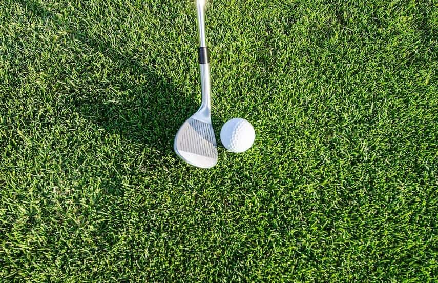 Head of a golf club next to golf ball on grass