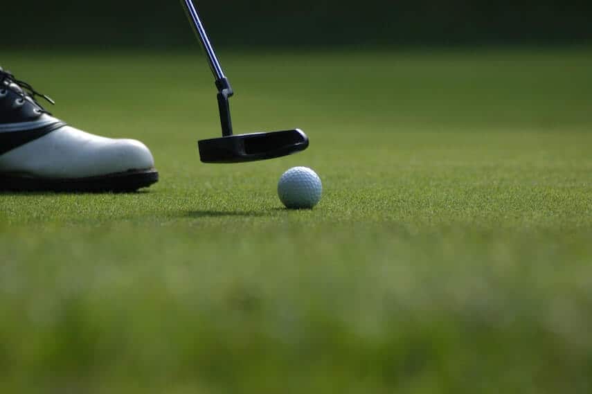 Head of a putter next to a gold ball on a putting green