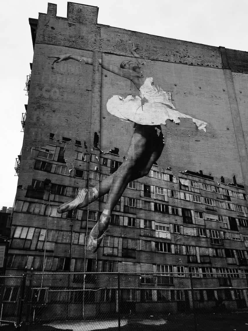 Large street art mural of a ballerina leaping in front of an apartment building painted on the wall