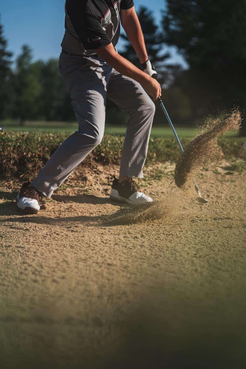 Male golfer swinging a club in a sand bunker, flicking sand up
