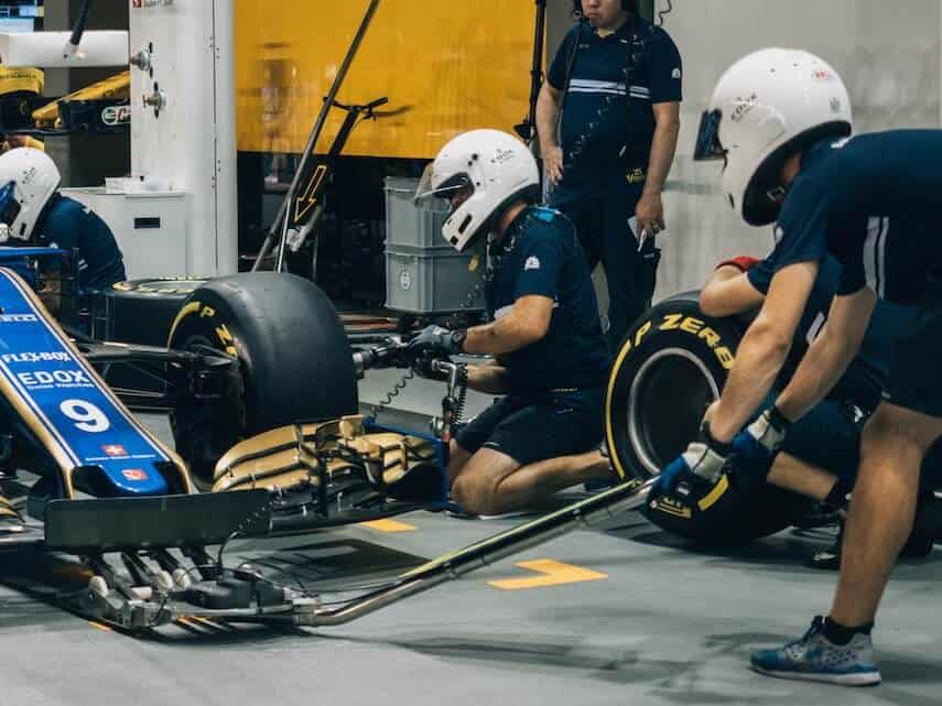 Mechanics wearing white helmets working on an F1 car in the pit lane