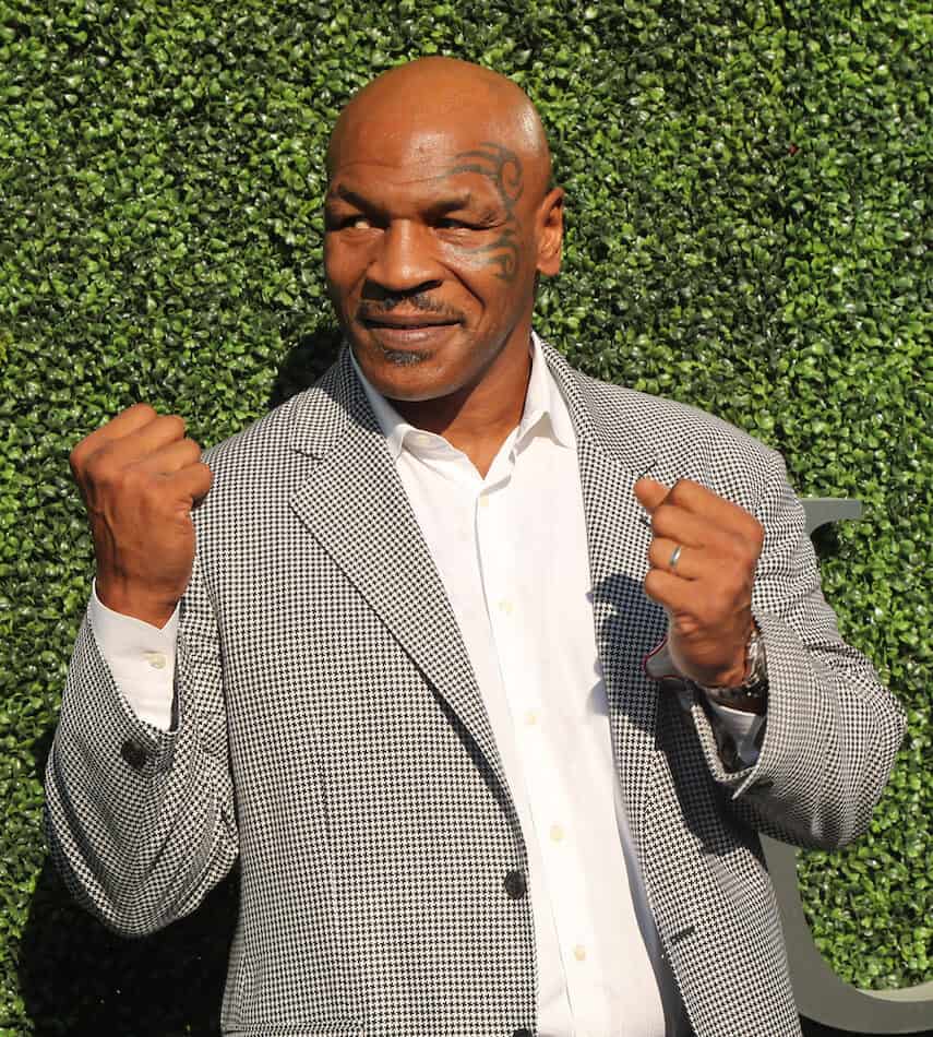 Mike Tyson with raised fists in front of a fake grass wall