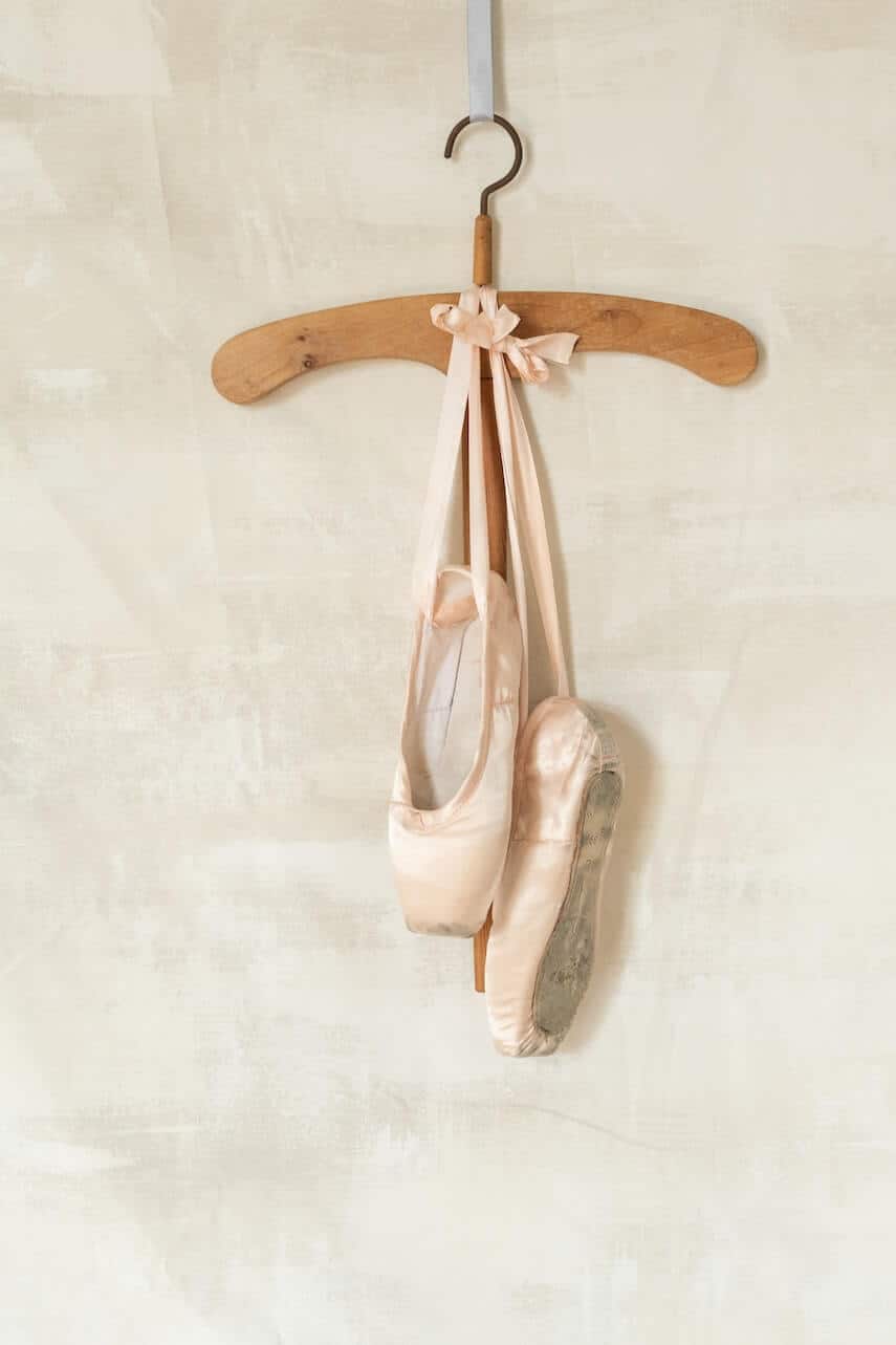 Pink pointe shoes hanging from a wooden hanger