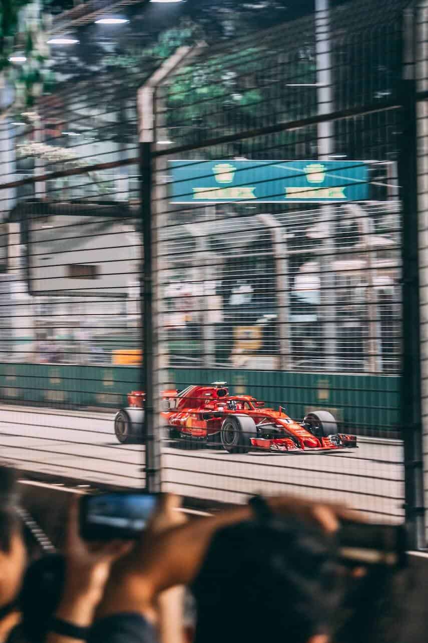 Red Ferarri streaming past fans in the stands behind silver safety cage wires