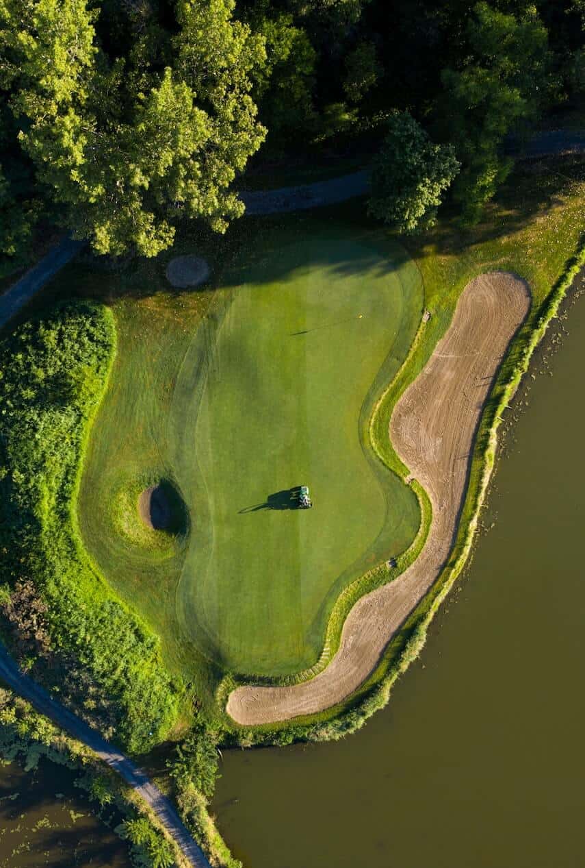 Top down shot of a putting green, a sand trap running along the side, next to lake