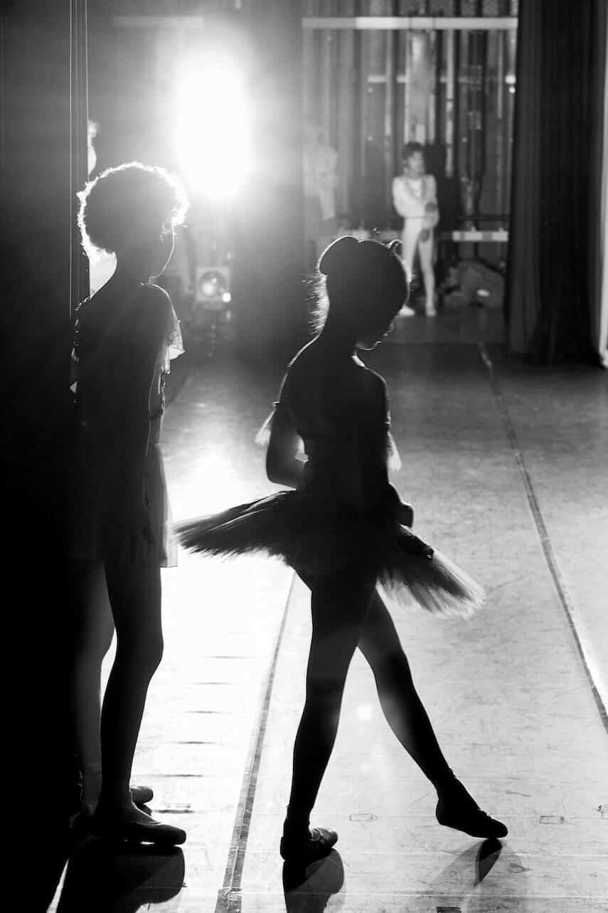 Two child ballerinas waiting in the stage wings with bright lights behind them