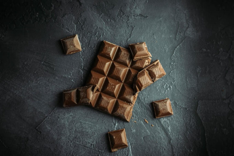 Chocolate Quiz Questions and Answers cover photo of a Block of squares of brown chocolate, individual squares broken off and resting on the large block