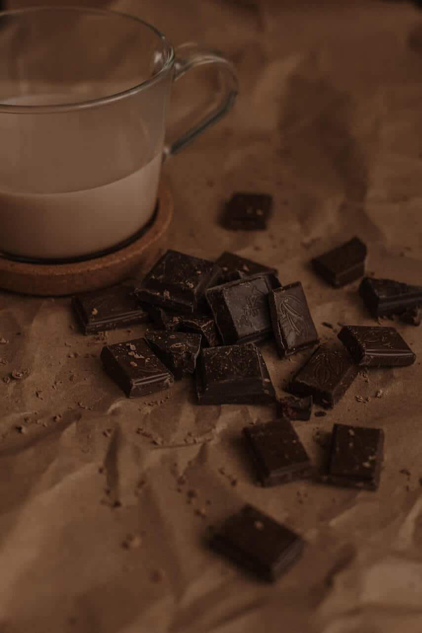 Clear glass mug of hot chocolate with squares of dark chocolate scattered next to it