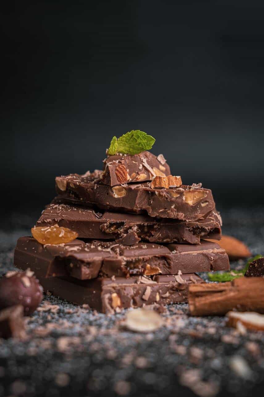 Thin blocks of chocolate with nuts embedded, stacked into a small pile, topped with a mint leaf