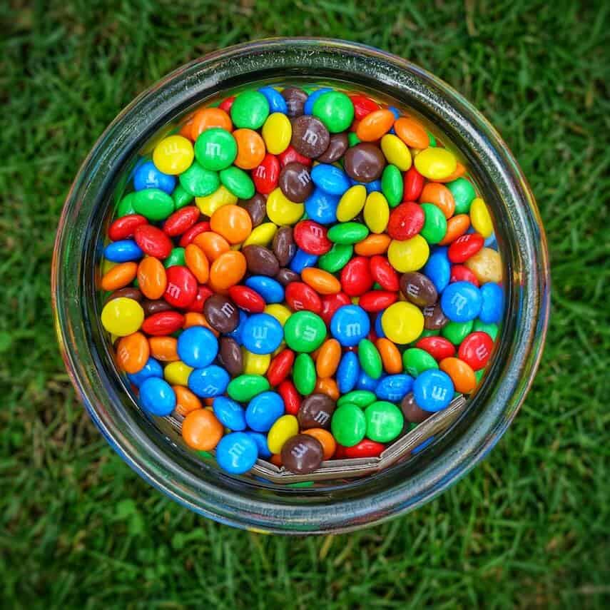 Top down shot of a glass jar of multicoloured M&Ms sitting on the grass