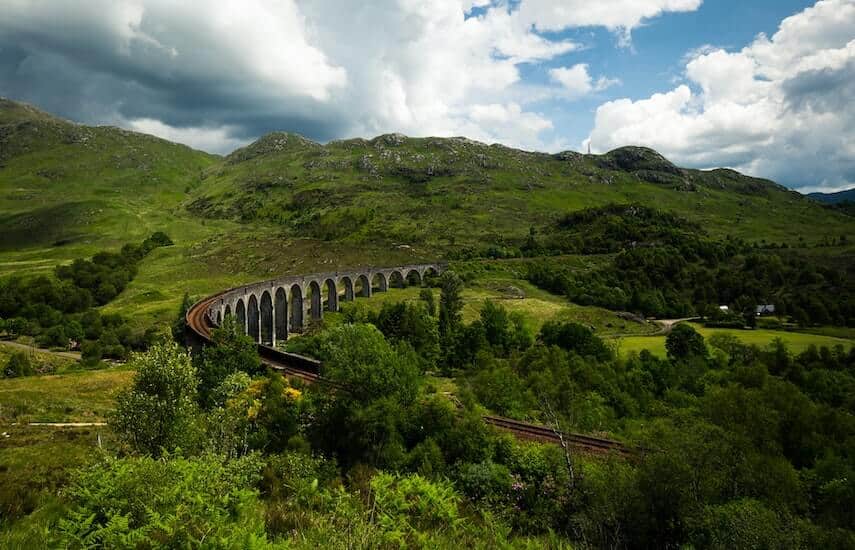 Glenfinnan Viaduct, Scotland - train track elevated over multiple stone arches surrounded by green hills