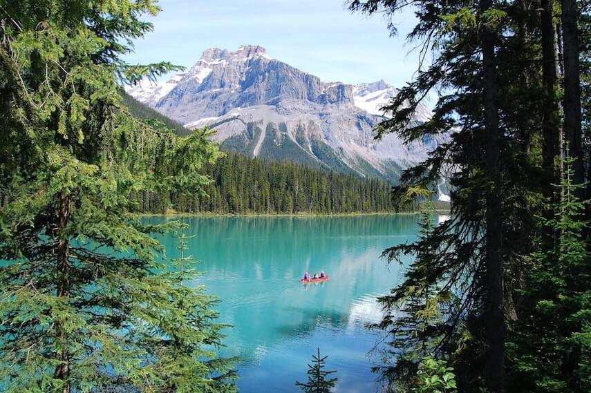 Aquamarine Emerald Lake in Canda with fir trees along the shore, a red canoe paddling on the lake and rocky mountains in the background