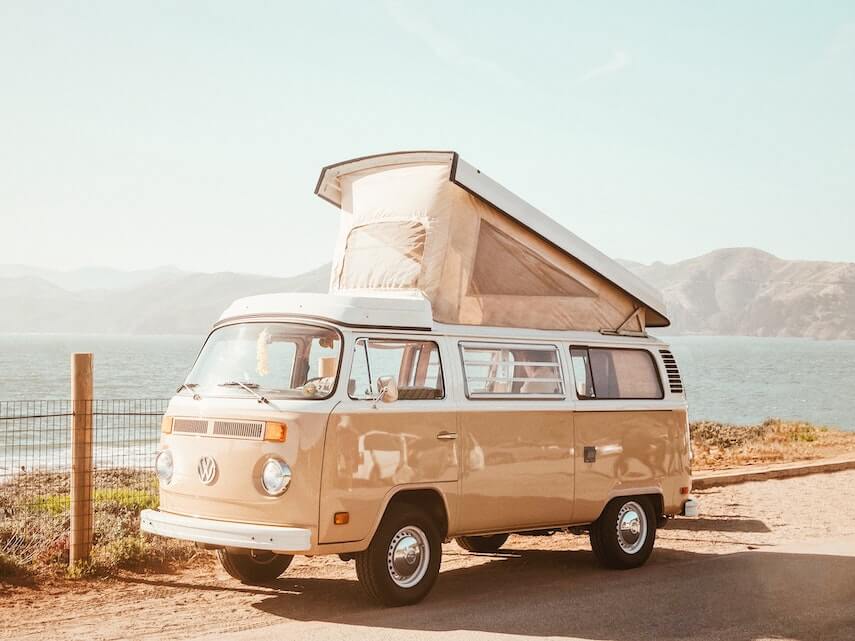 Beige VW camper with a popped tent top parked in front of the ocean