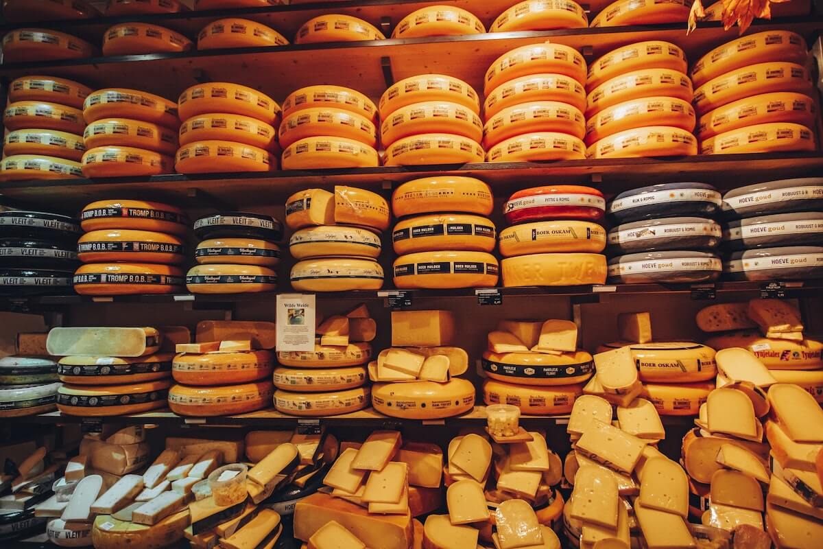 Cheese Quiz Questions and Answers cover photo of yellow and orange wax coloured wheels of cheese on wooden sheleves