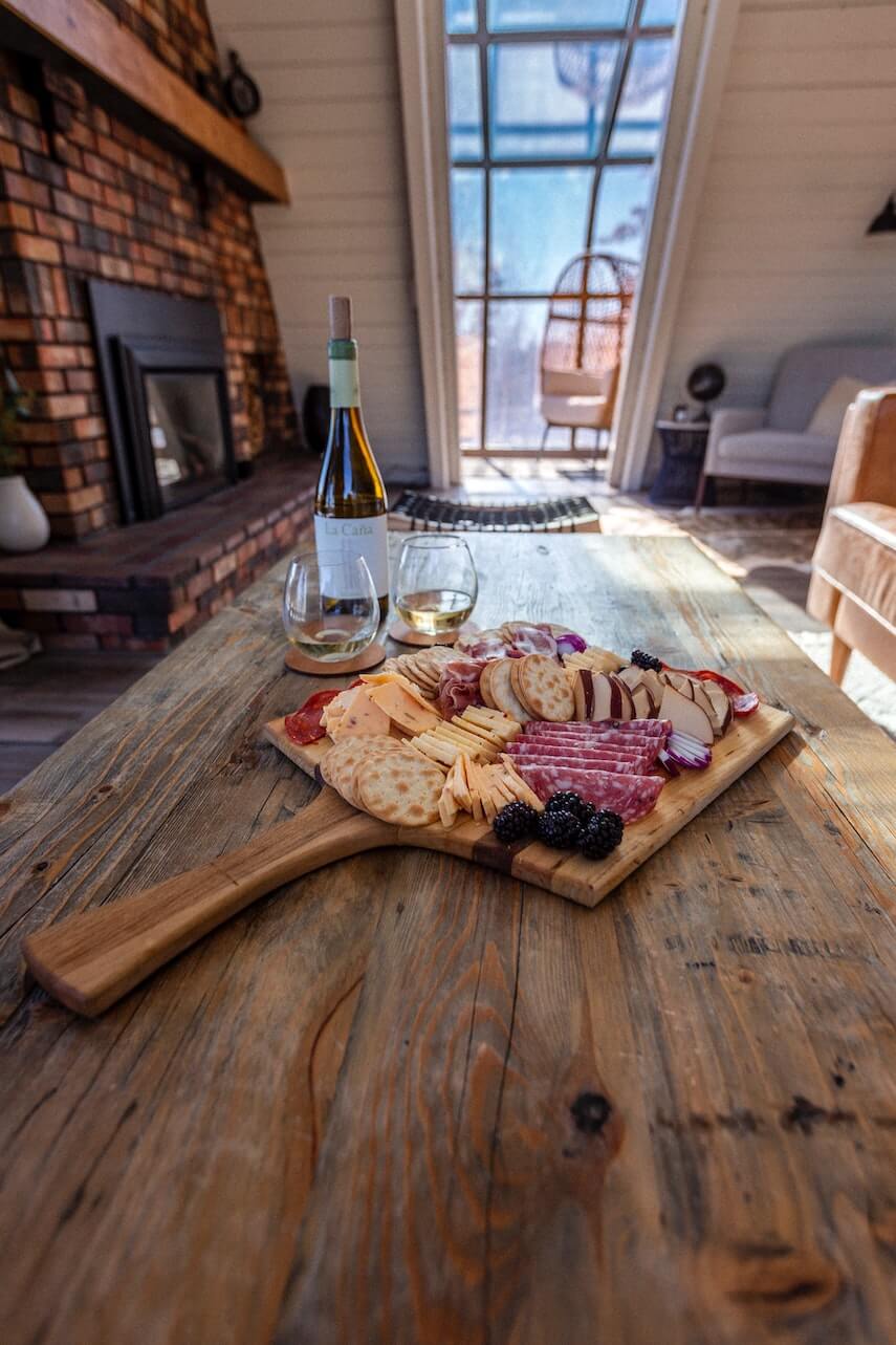 Cheeseboard with bottle of wine and 2 glasses on a wooden table in a living room