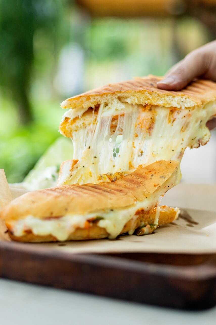 Cheesy panini, half being raised, the cheese stretching upwards