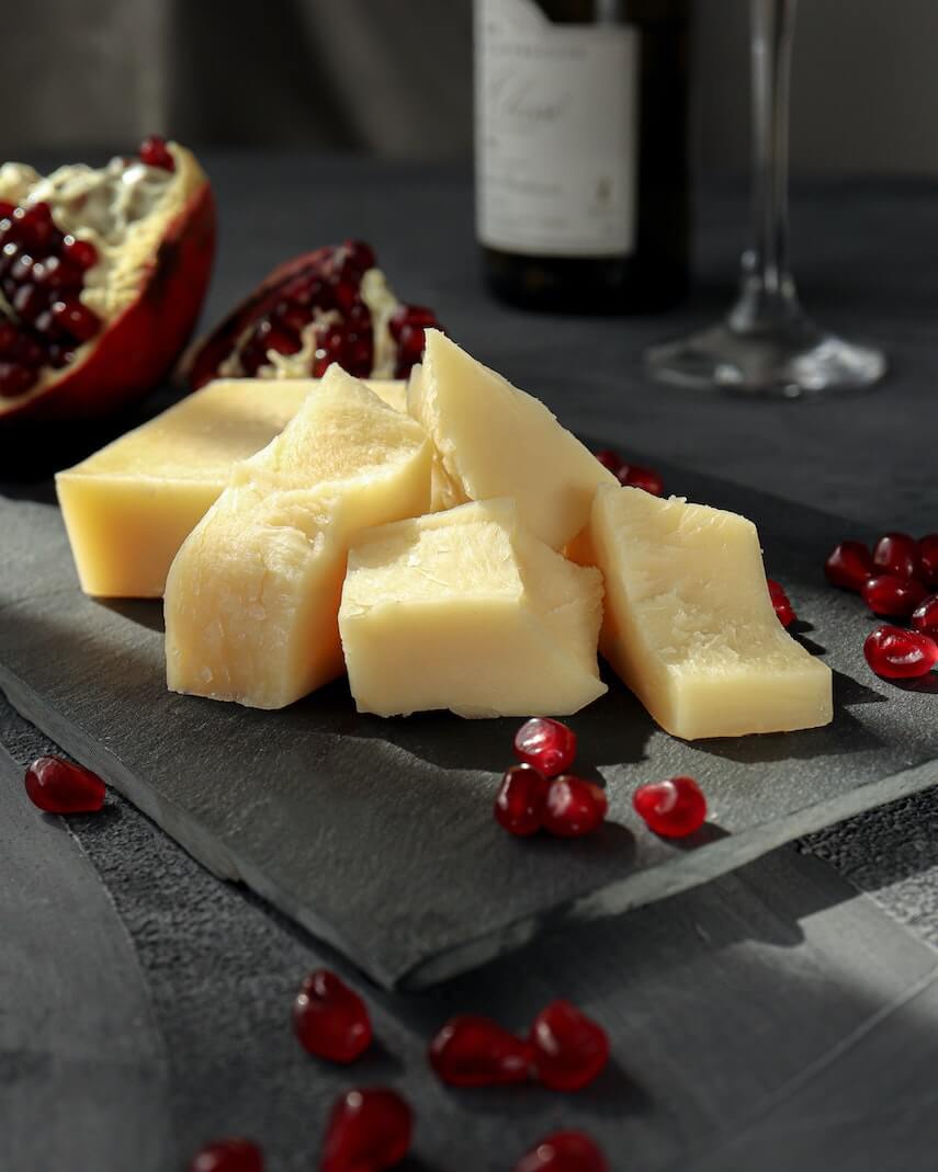 Hard cheese on a black slate surrounded by pomegranate pearls