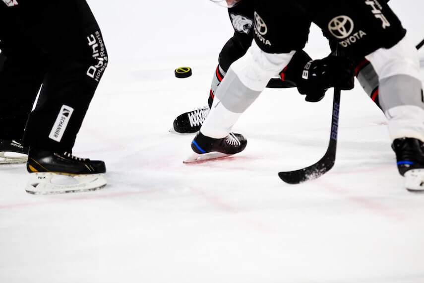 Legs of two men ice ice hockey sticks fighting for a puck, next to the legs of an umpire