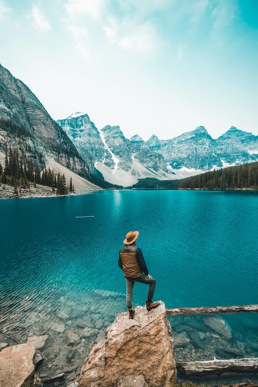 Man standing on a rock in front of Moraine Lake with the Canadian Rockies in the background