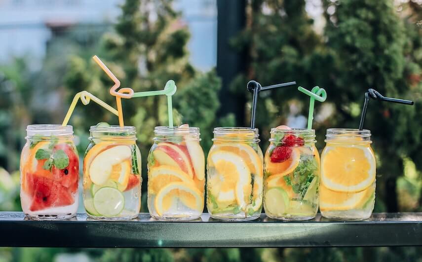 Mason jars with fruity cocktails on a black ledge with trees in the background