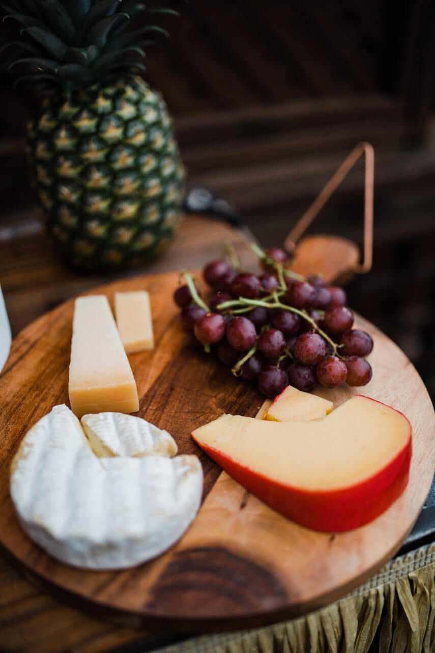 Round cheese board with brie, edam and hard cheddar cheese next to purple grapes