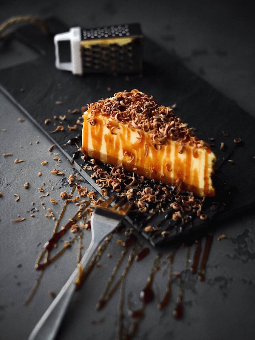 Slice of cheesecake on a black slate with a mini cheese grater as decoration