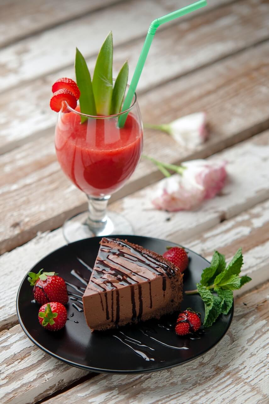 Slice of chocolate cake on a black plate, with strawberries either side