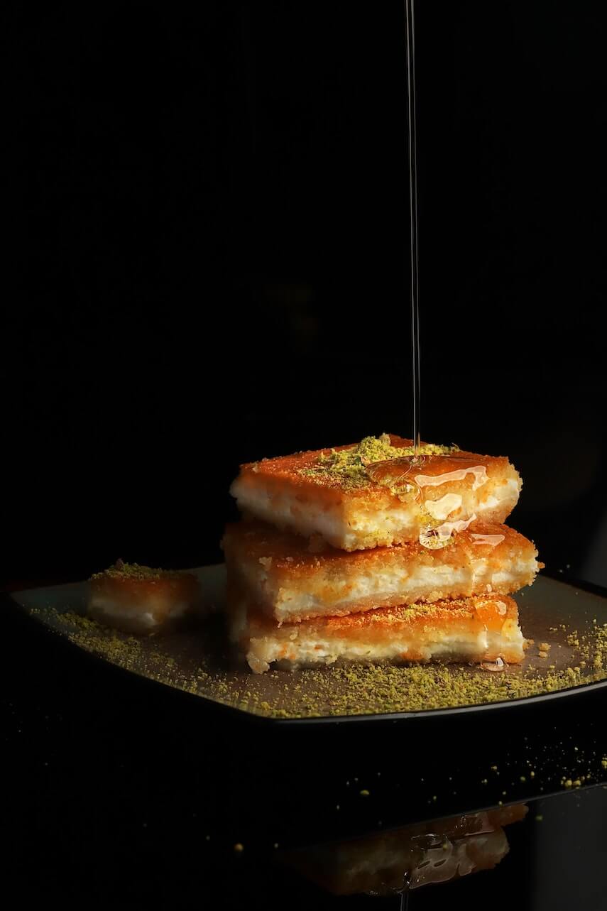 Slices of baklava, dusted with crushed pistachio with a drizzle on honey being poured on top