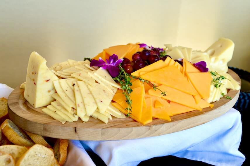 Slices of cheese on a wooden board, grapes and flowers at the centre