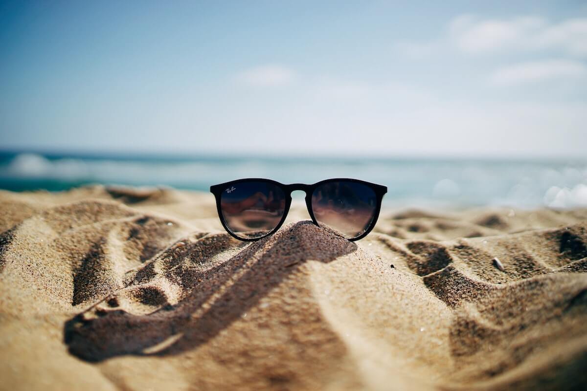 The Ultimate Summer Quiz cover photo of sunglasses on sand in front of the ocean