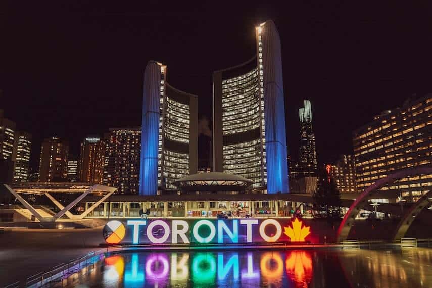 Toronto sign lit up in multiple colors in front of the city skyline