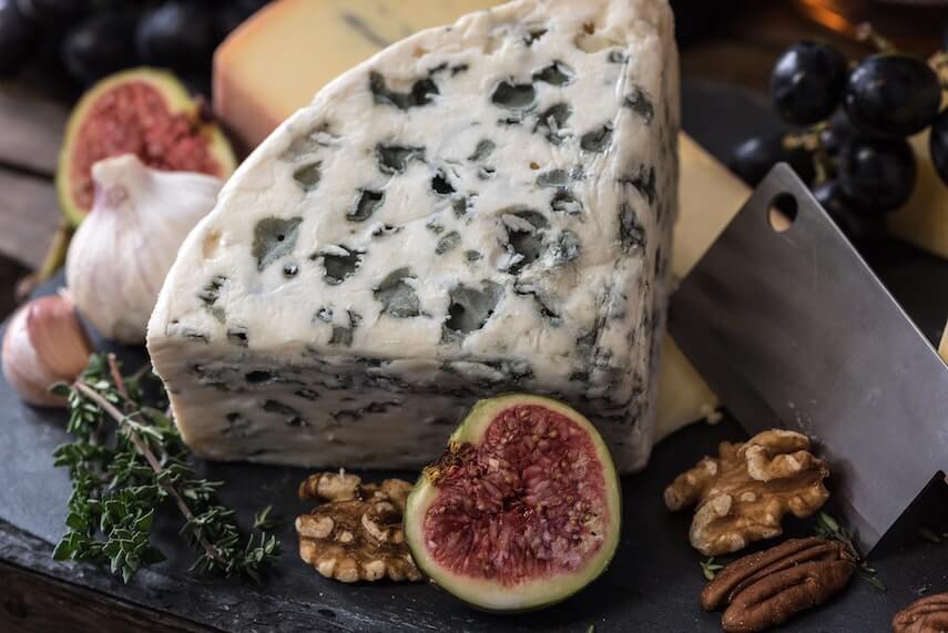 Wedge of blue cheese with cut figs and nuts next to it