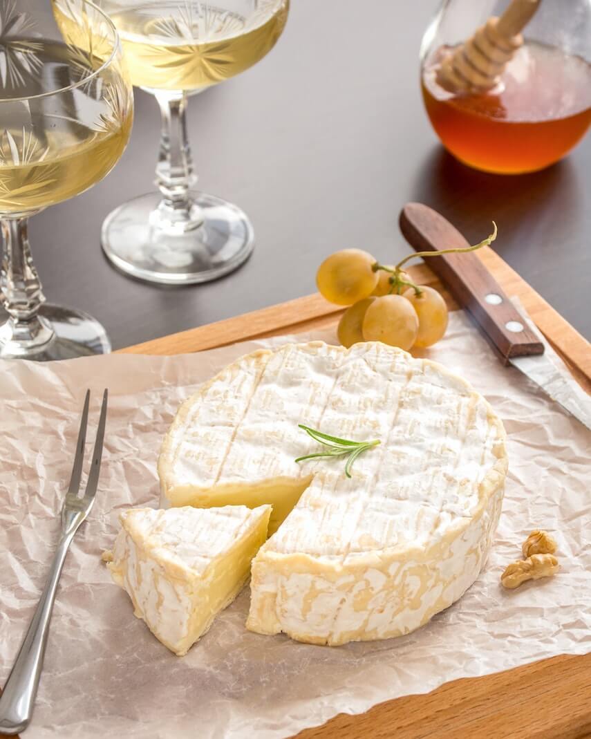 Wheel of Brie on paper, a wedge cut out, next to two glasses of wine