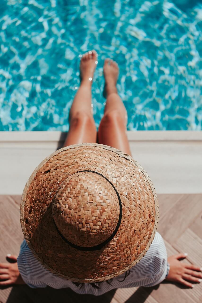 Woman wearing a striped shirt and a straw hat sitting on the edge of a swimming pool