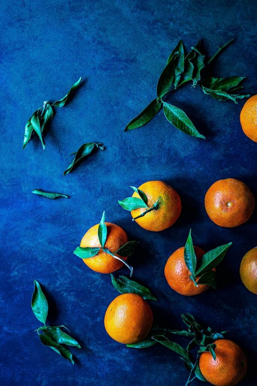 5 oranges, with leaves attached on a blue table