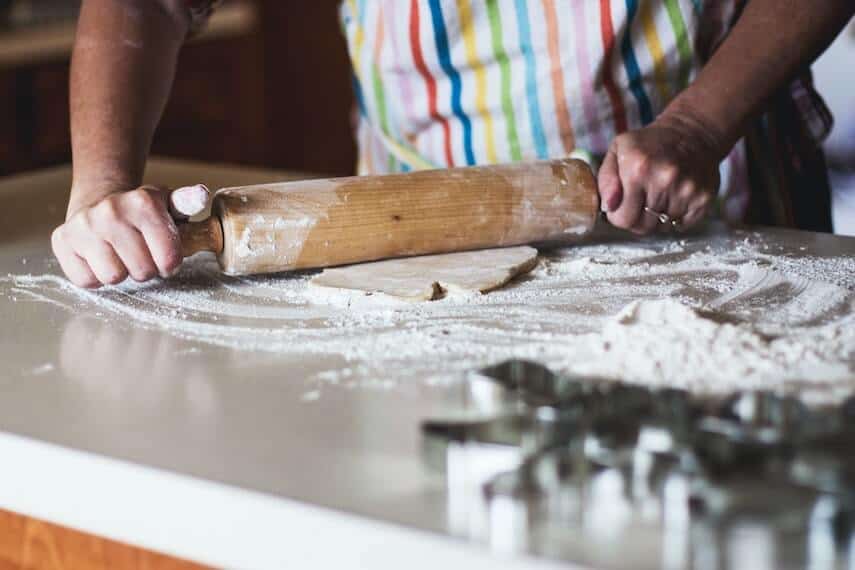 Body of a person wearing a striped apron,using a rolling pin on dough on a marble bench