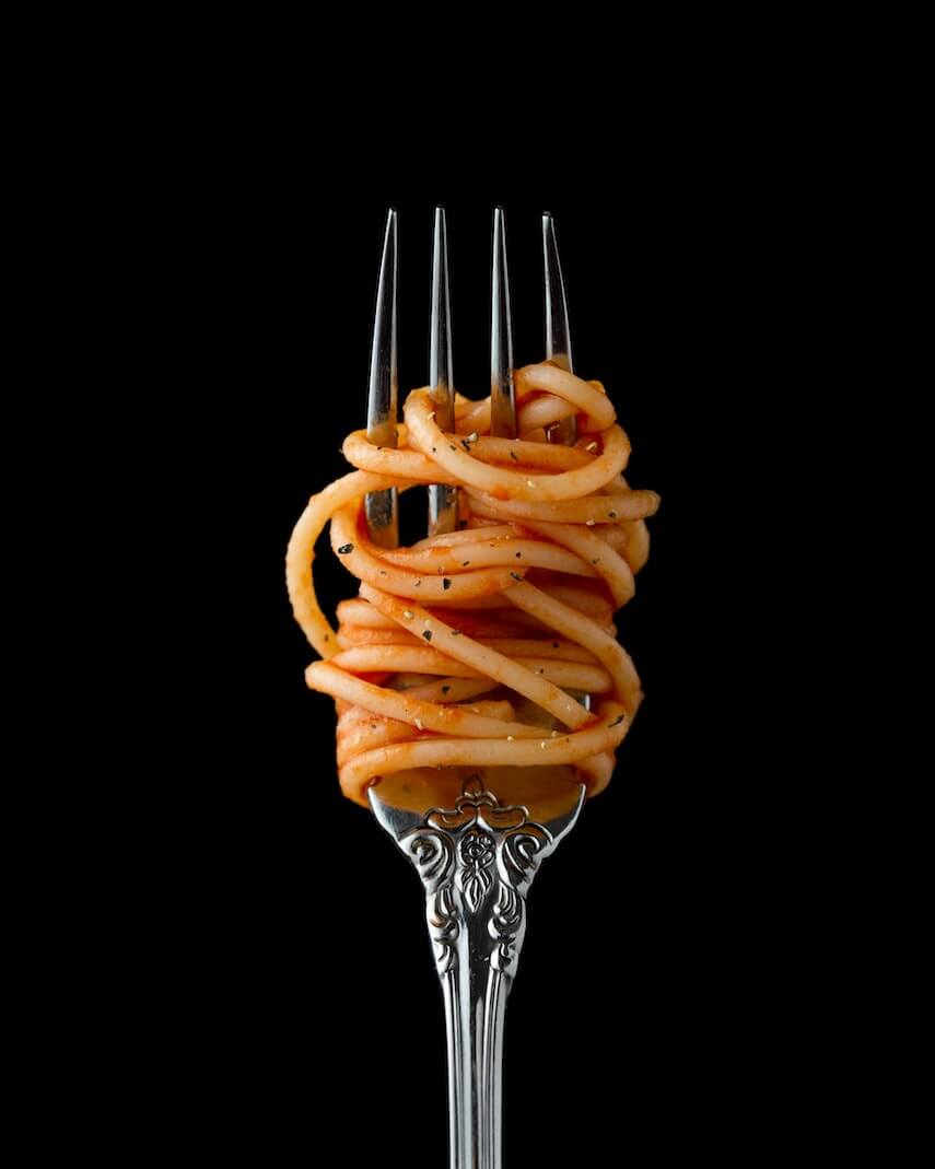 Cooked spaghetti twirled around a silver fork in front of a black background