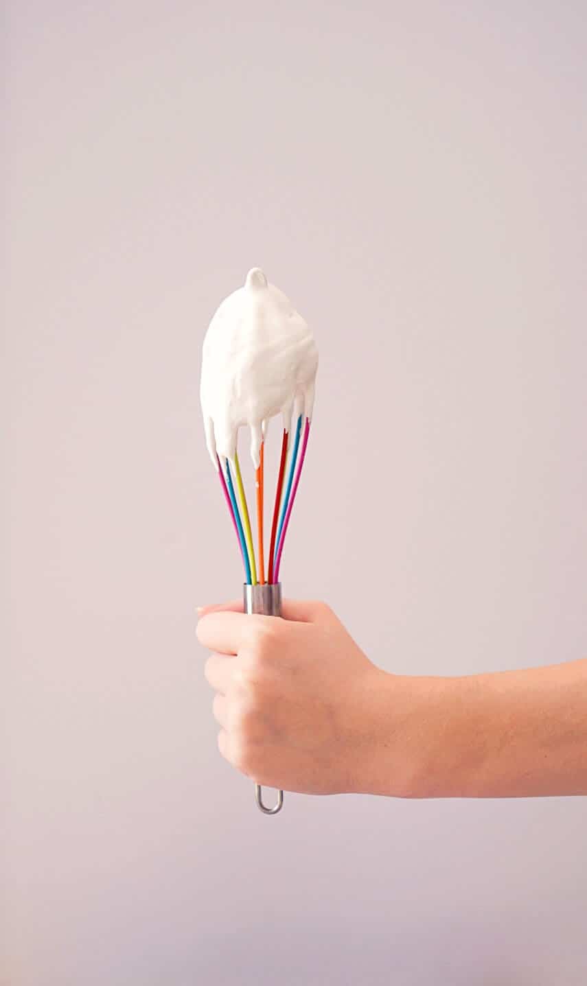 Hand holding a multicoloured whisk covered in stiff cream